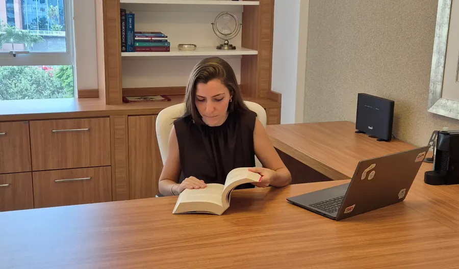 Carolina Cervone lendo um livro na mesa do consultório