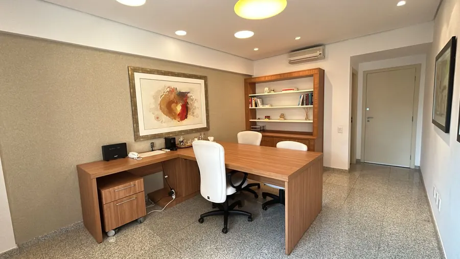 Mesa de atendimento com cadeiras brancas, quadro e estante de livros